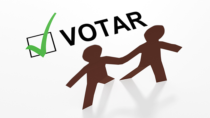 Two paper people of color with a Spanish votar checkbox and a green checkmark in a 3d illustration.